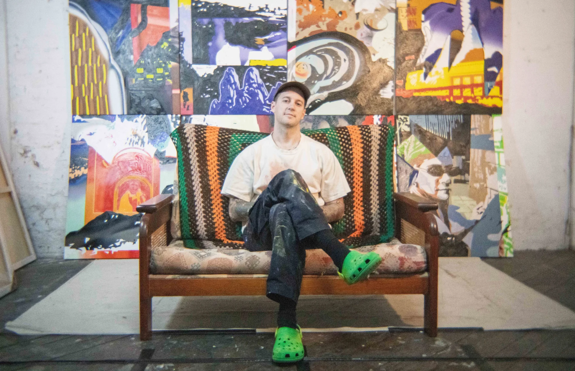 Aaron Ashworth sitting in front of his artwork in PS art space, Fremantle
